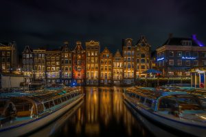 Beautiful lit houses along the canal at Damrak street, tourist boats in front, night scene, colorful